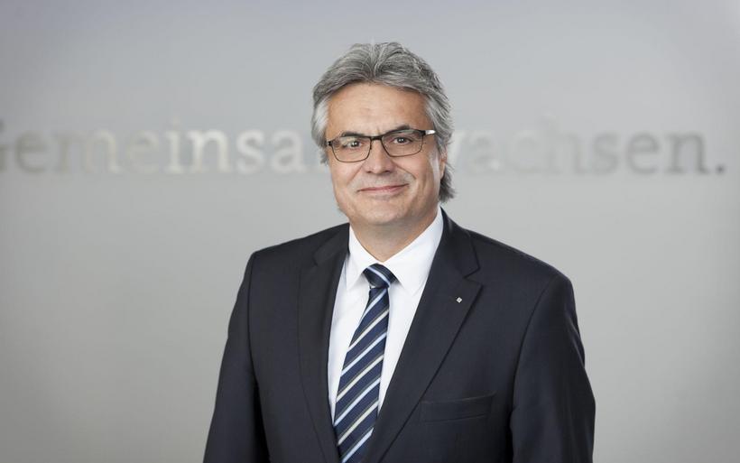 Portrait eines Mannes mittleren Alters mit grauen Haaren und heller Hautfarbe. Er trägt eine Brille und einen Anzug.