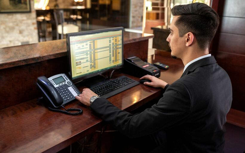 Empfangsmitarbeiter, der hinter einer Rezeption sitzt und auf seinen Monitor schaut