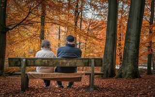 Rentnerpaar sitzt im herbstlichen Wald auf einer Bank.