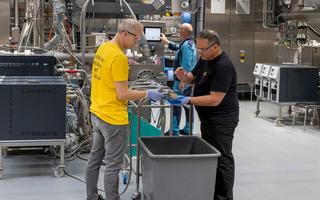 Zwei Männer hantieren in einer Produktionsstätte mit einem Schlauch.