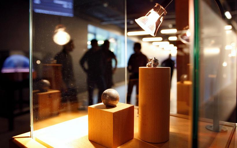 In einem gläsernen Austellungskasten befindet sich ein rundes Objekt. Im Hintergrund sind Menschen sichtbar.