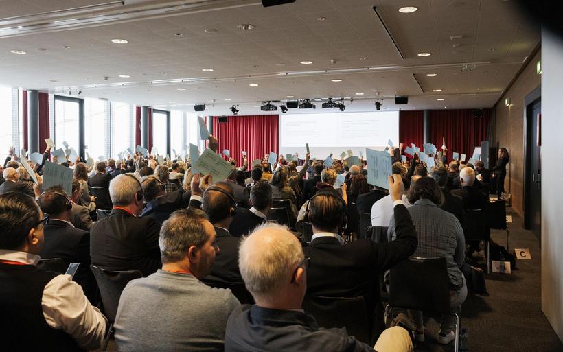 Menschen sitzen in einem Saal und stimmen ab