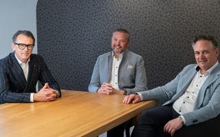 Drei Männer sitzen an einem Tisch vor einer schwarzen Wand